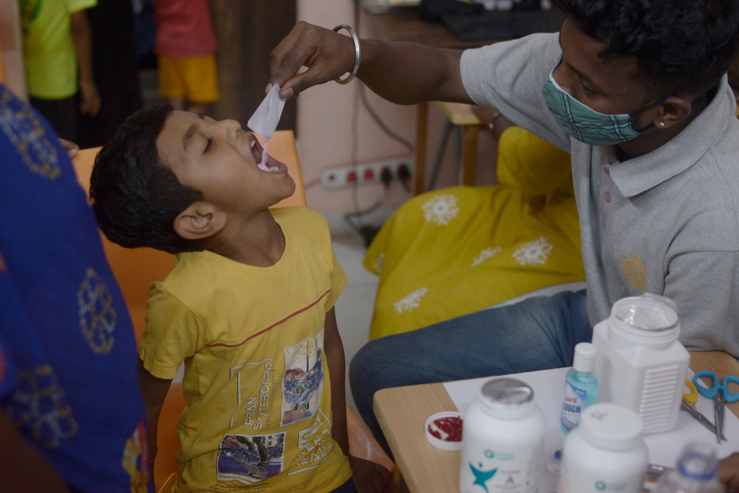A masked health worker gives a child a vitamin dose during a routine screening.