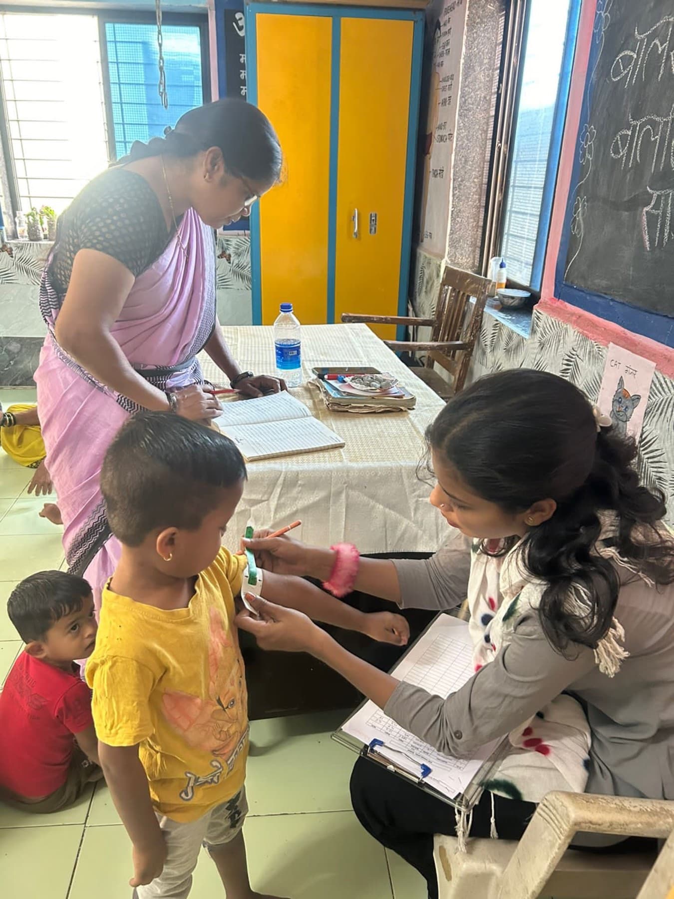 A health worker measures a child's arm and logs the reading. This routine screening runs alongside every serving.