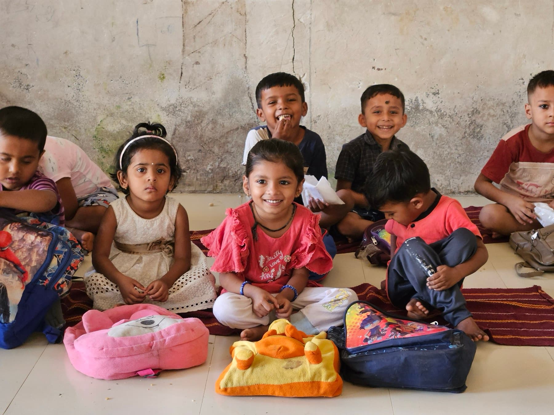 Young children sit together on the floor of their anganwadi, smiling for the camera.